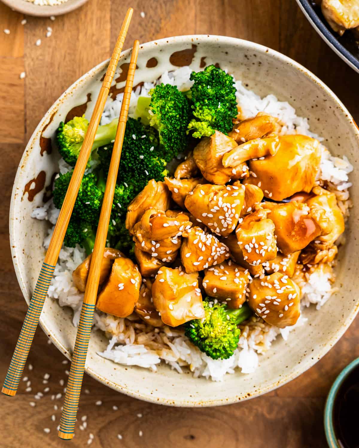 overhead view of teriyaki chicken in a white bowl with rice and broccoli and chopsticks.