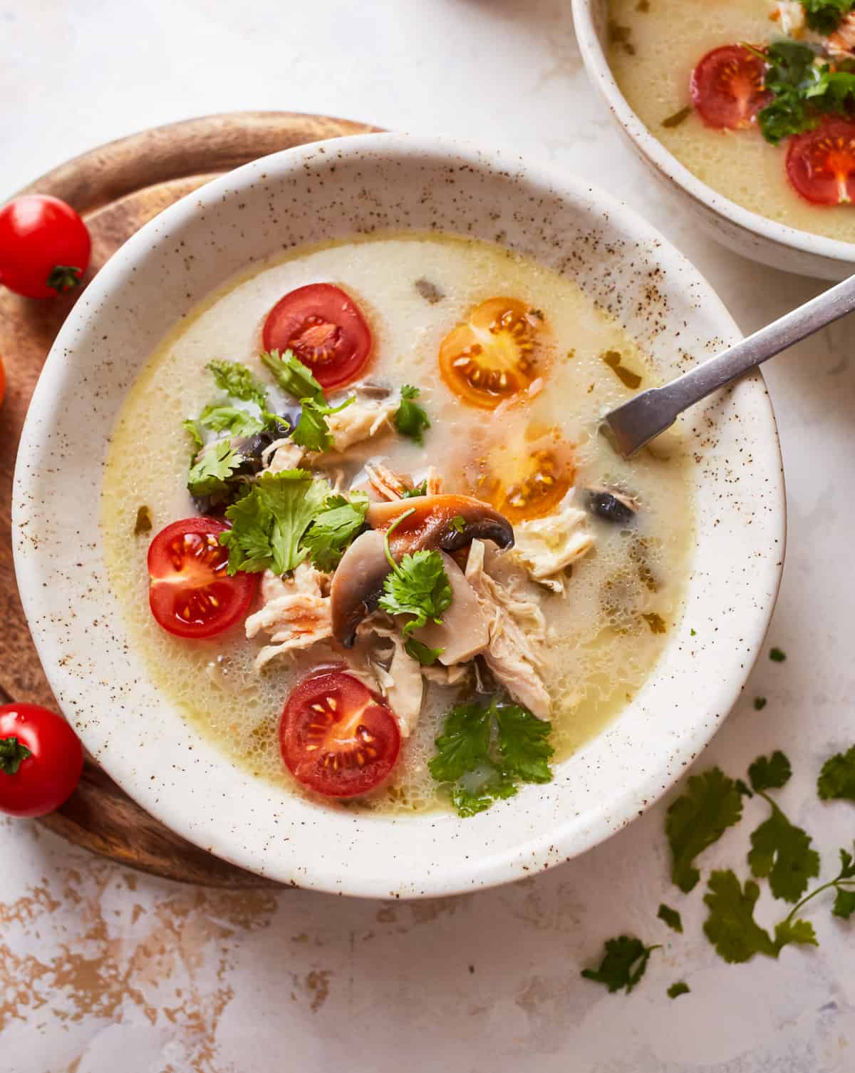 overhead view of a serving of Thai coconut chicken soup in a white bowl with a spoon.