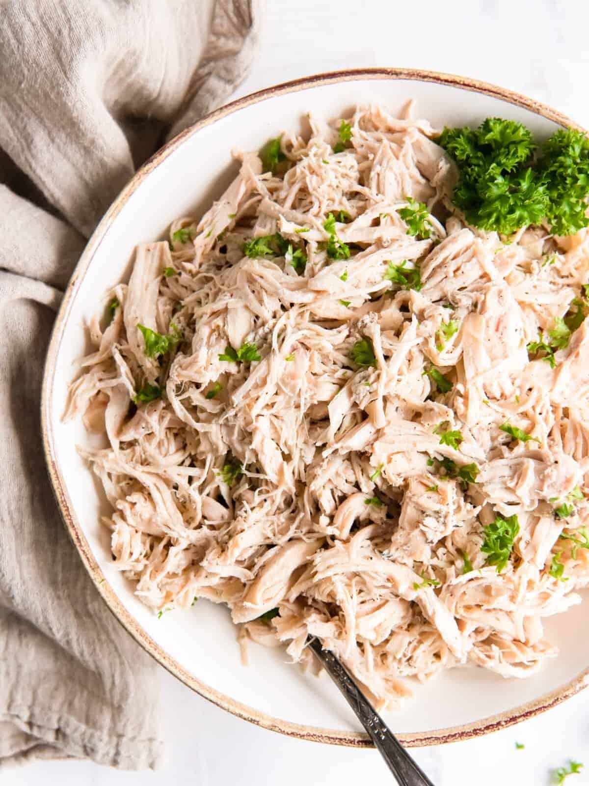 crockpot shredded chicken in w white bowl with a fork.