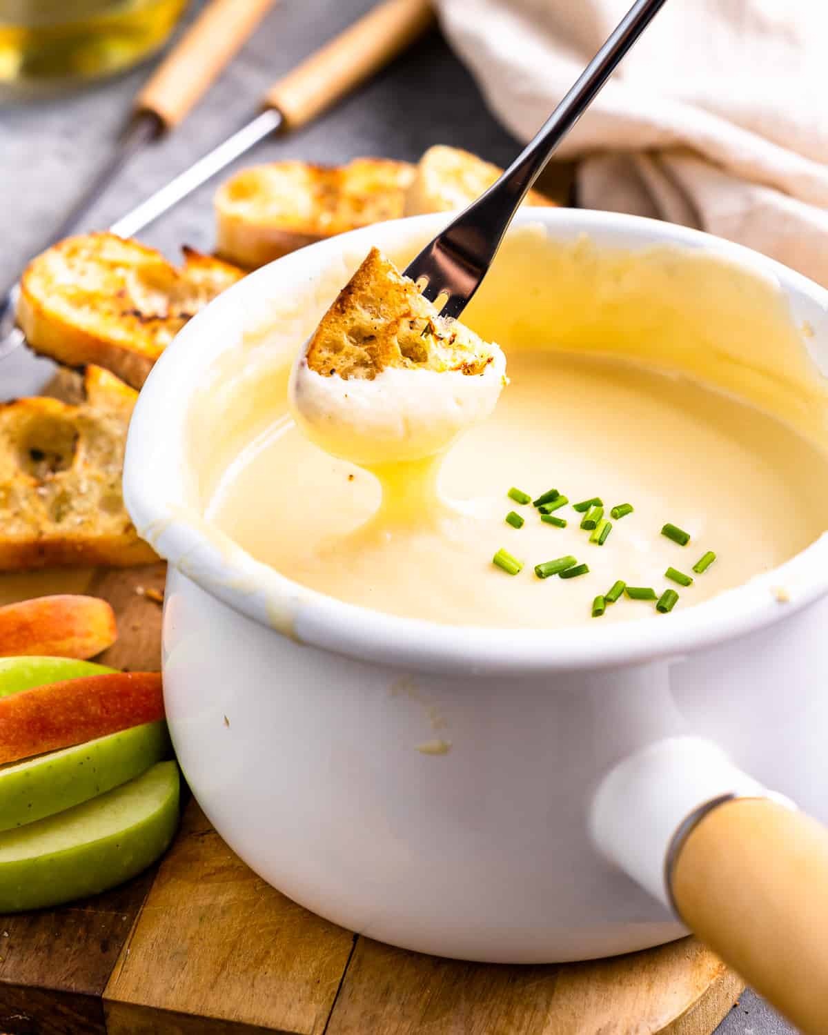 three-quarters view of a piece of grilled bread being dipped into a pot of fondue with a long fork.