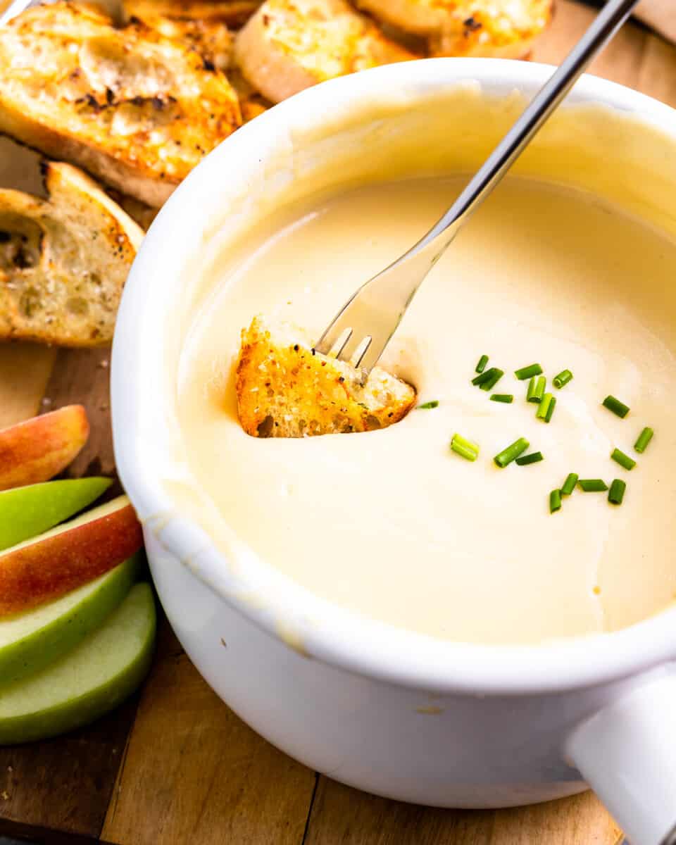 overhead view of a long fork dipping grilled bread into a pot of cheese fondue.