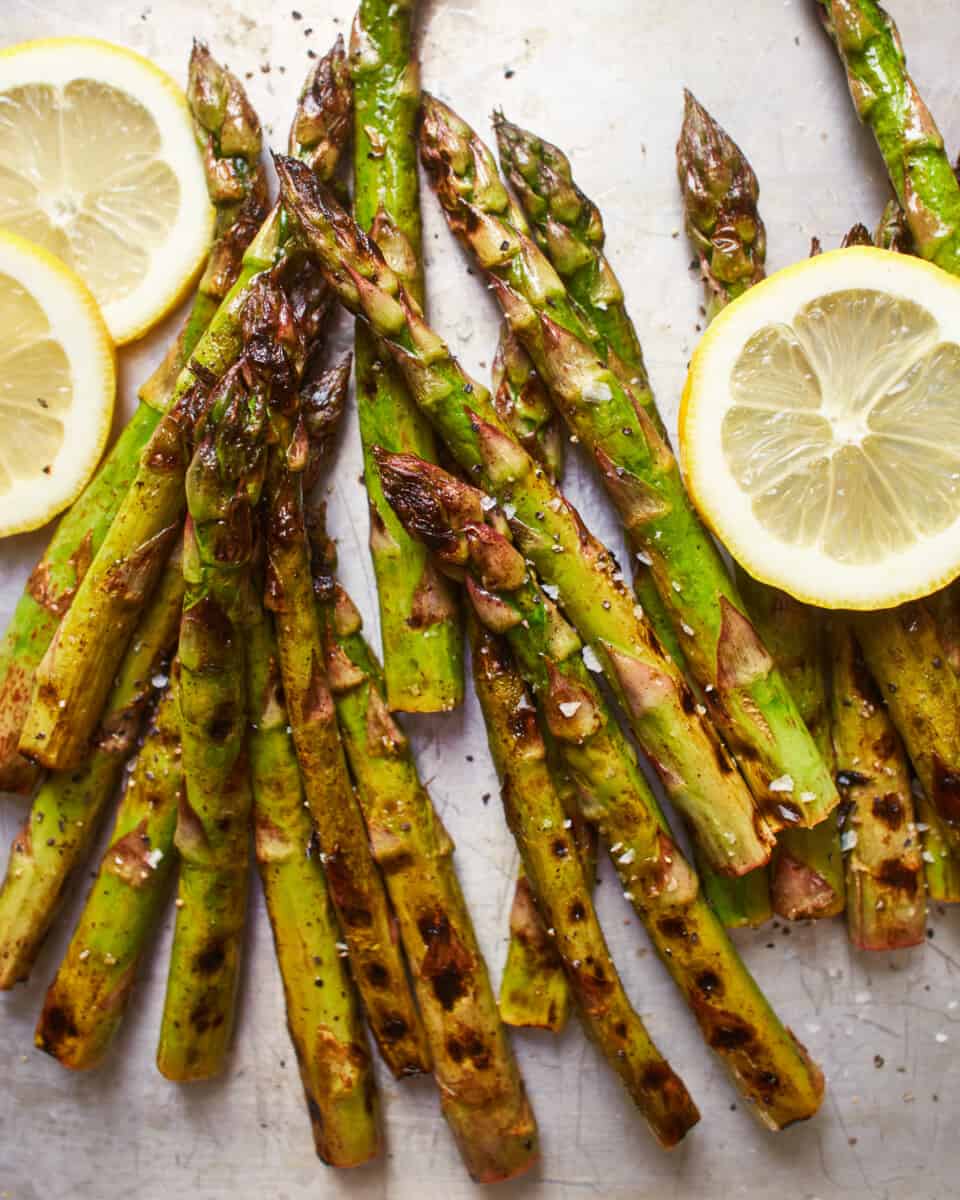 close-up overhead view of grilled asparagus on a baking sheet with lemon wheels.
