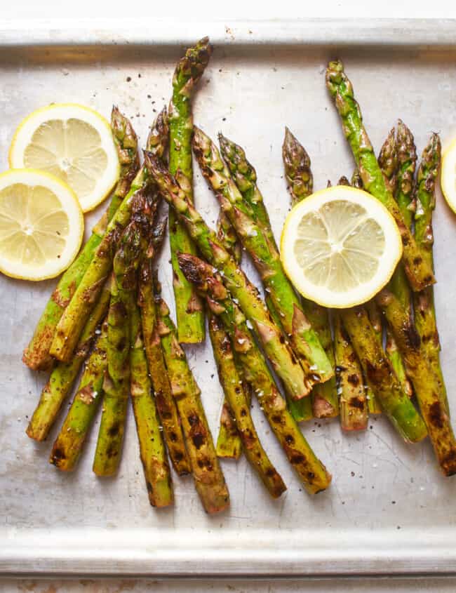 overhead view of grilled asparagus on a baking sheet with lemon wheels.