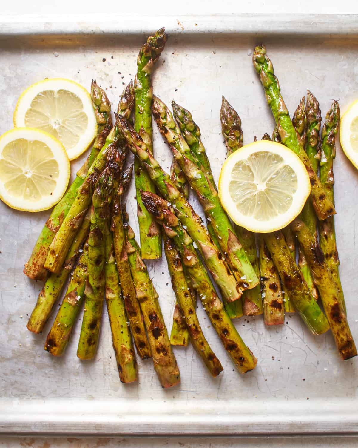 overhead view of grilled asparagus on a baking sheet with lemon wheels.