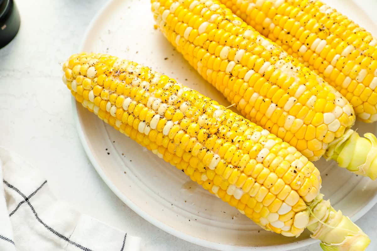 close up overhead view of 3 grilled corn cobs on a white plate.