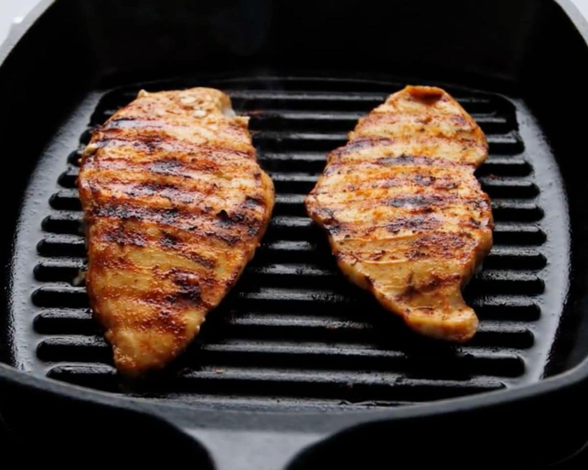 Marinated chicken breasts cooking on a grill pan with visible grill marks forming on the surface.