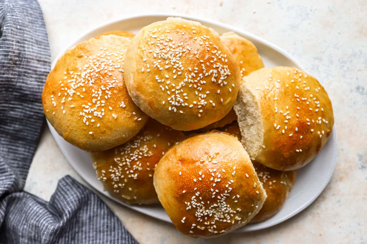 homemade hamburger buns with sesame seeds on a plate.