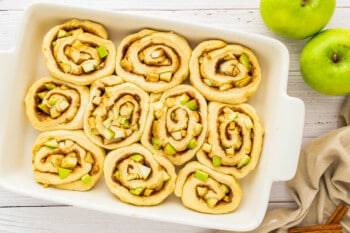 apple cinnamon rolls in a white dish on a wooden table.