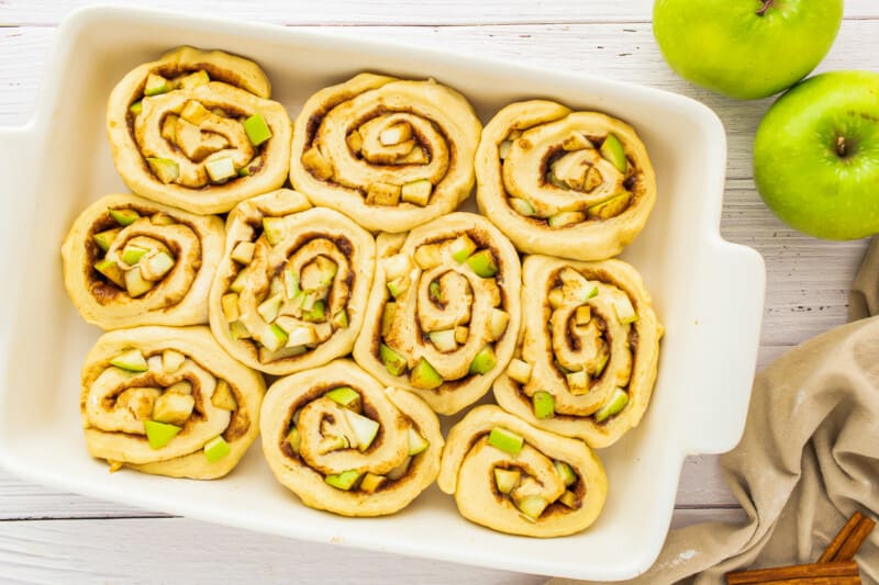 apple cinnamon rolls in a white dish on a wooden table.