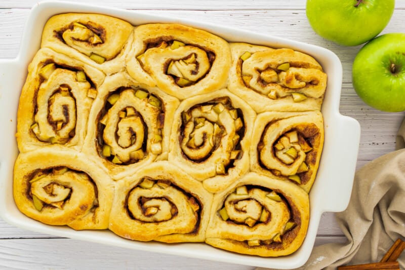 apple cinnamon rolls in a white dish on a wooden table.