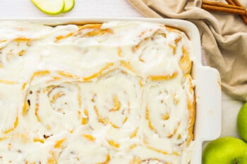 apple cinnamon rolls in a white dish with cinnamon sticks.