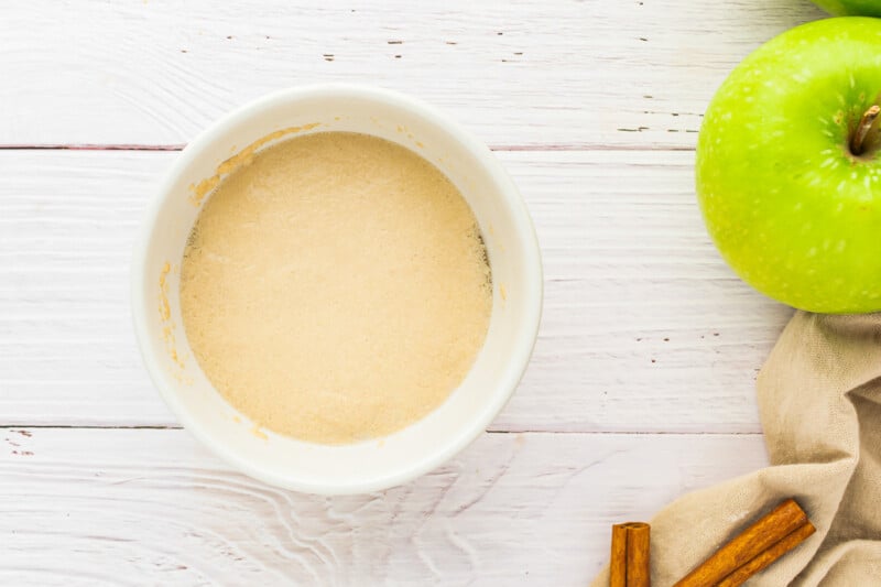 a white bowl with apples and cinnamon next to it.