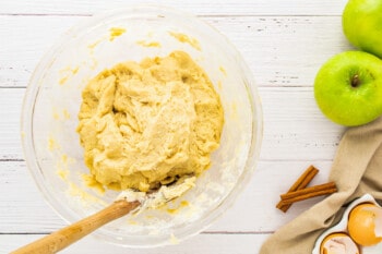 a bowl of dough with apples and cinnamon next to it.