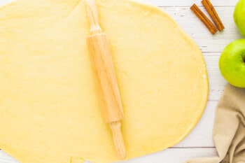 a rolling pin and apples on a wooden table.