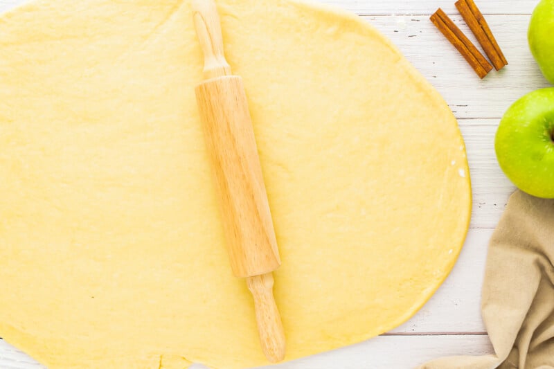 a rolling pin and apples on a wooden table.