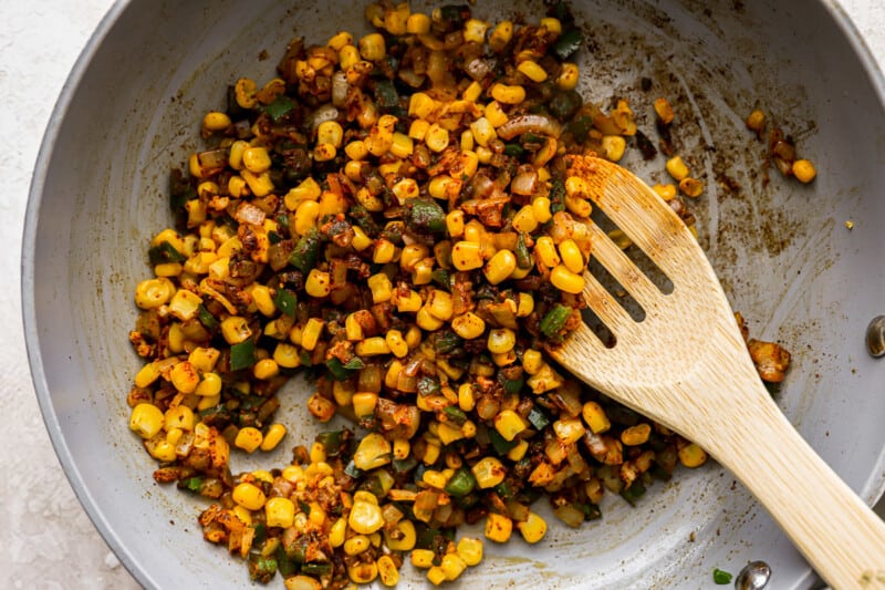 corn in a frying pan with a wooden spoon.