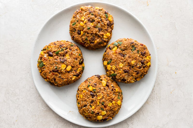 four black bean and corn burgers on a white plate.