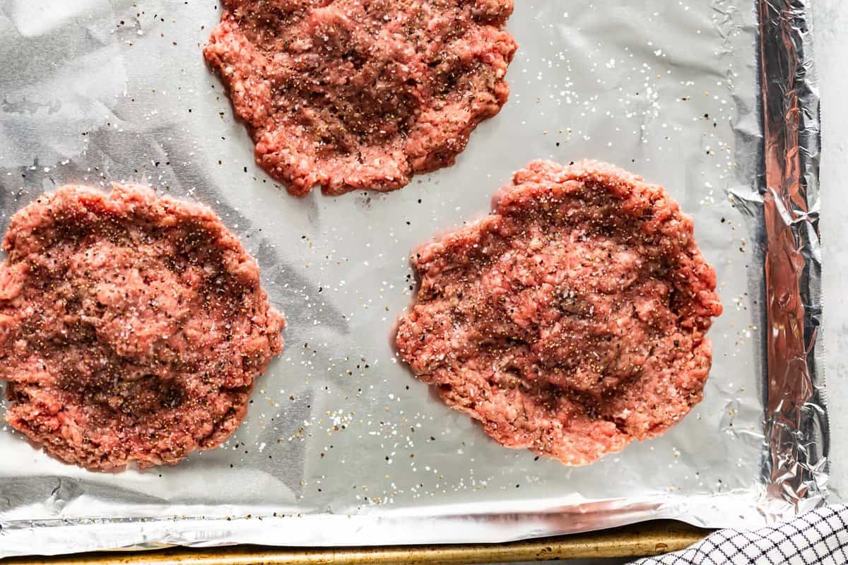 raw hamburger patties on a baking sheet