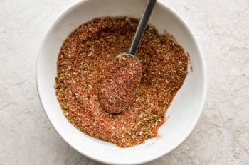 a white bowl of seasoning with a spoon in it.