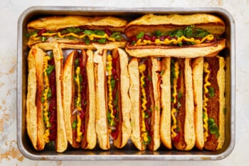 onions, cilantro, ketchup, and mustard in 8 hot dog buns in a baking pan.
