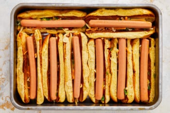hot dogs added to topping-filled hot dog buns in a baking pan.