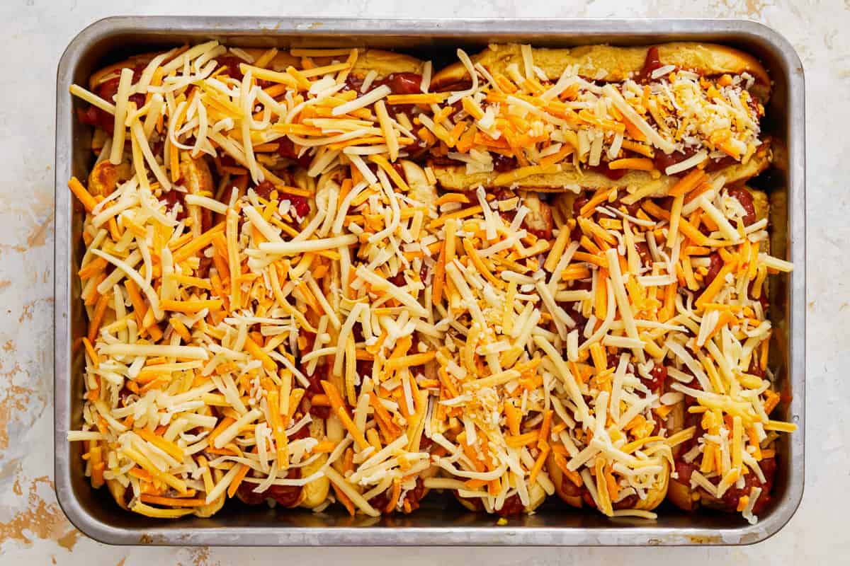 cheese sprinkled over chili dogs in a baking pan.