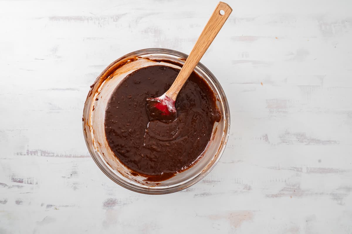 brownie batter in a glass bowl with a wooden spoon.