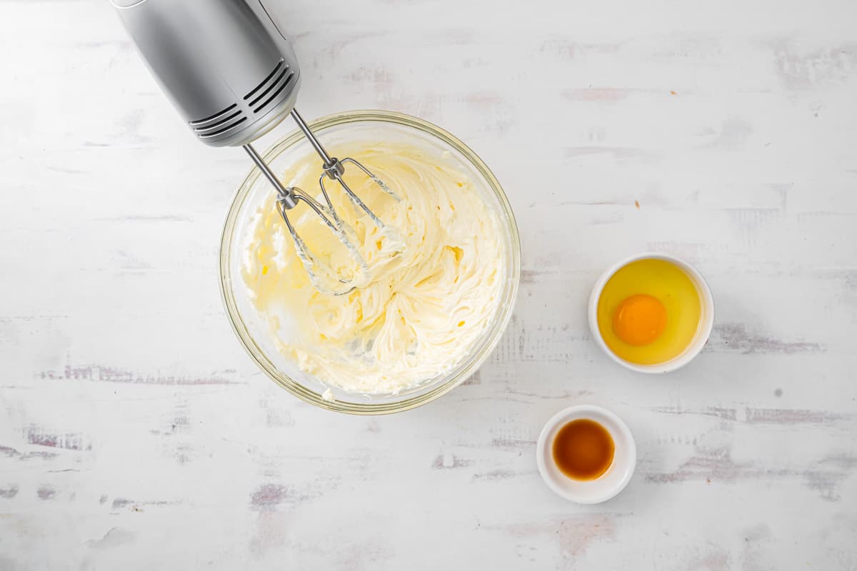 whipped cream cheese in a glass bowl with a hand mixer.