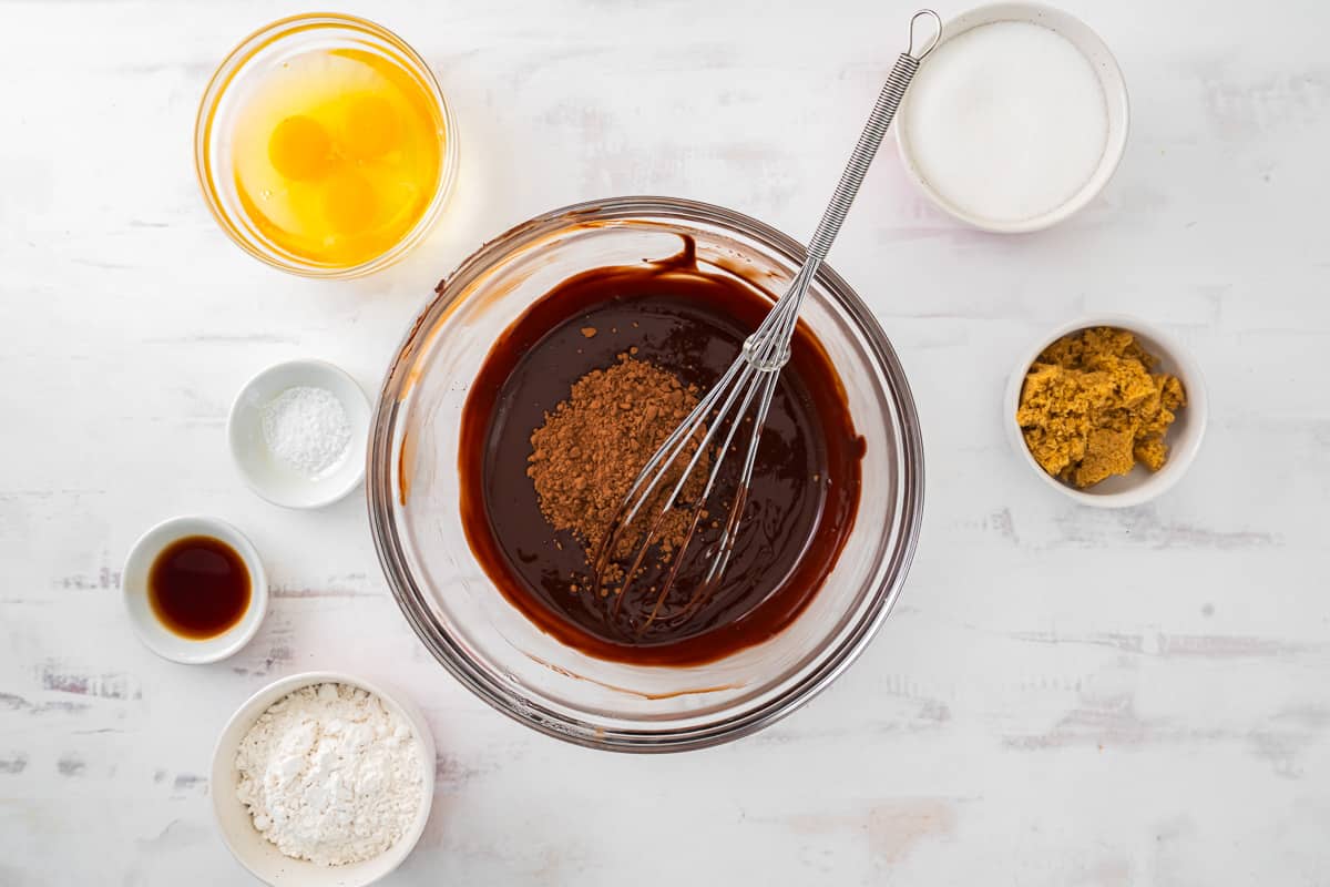 cocoa powder added to melted chocolate in a glass bowl with a whisk.