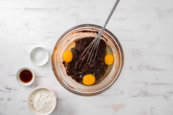 eggs added to sugar and chocolate mixture in a glass bowl with a whisk.