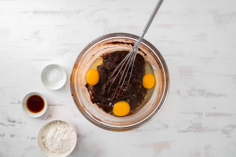 eggs added to sugar and chocolate mixture in a glass bowl with a whisk.