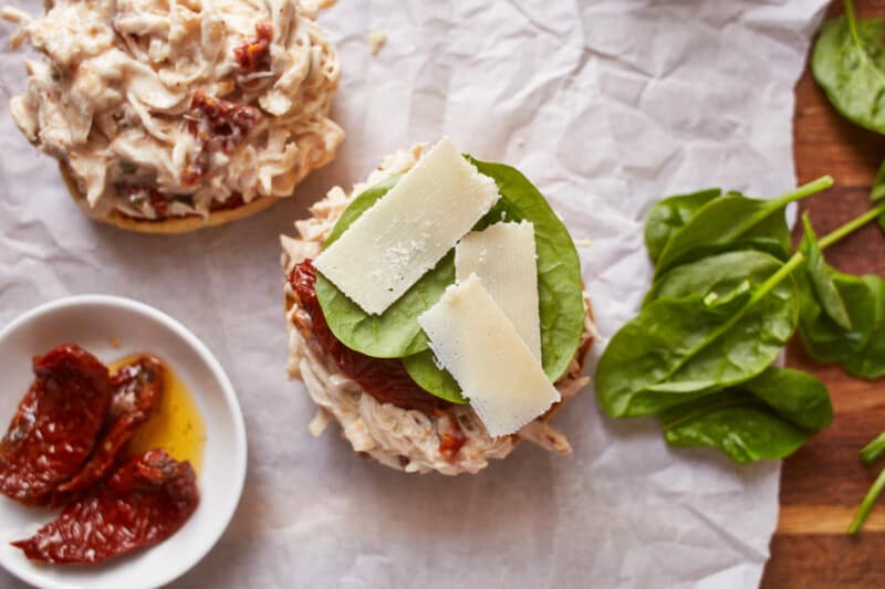 sun dried tomato, basil, and cheese on top of crockpot alfredo chicken on a sandwich bun.