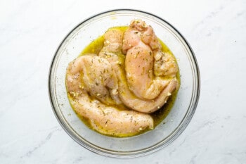 raw chicken breasts marinating in a glass bowl.