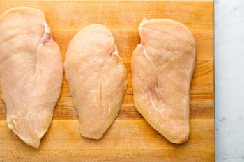 raw chicken breasts on a wooden cutting board.