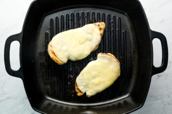melted cheese on top of grilled chicken in a grill pan.