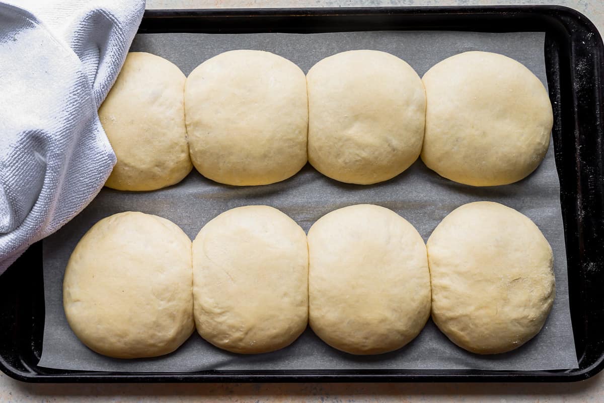 bread rolls on a baking sheet with a towel on top.
