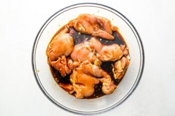 raw chicken thighs marinating in huli huli sauce in a glass bowl.