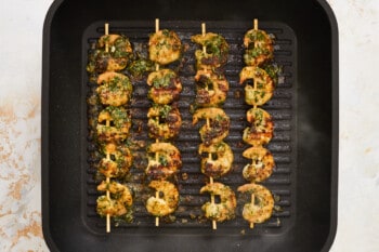 4 skewers of 5 each cooked pesto shrimp on a grill pan.