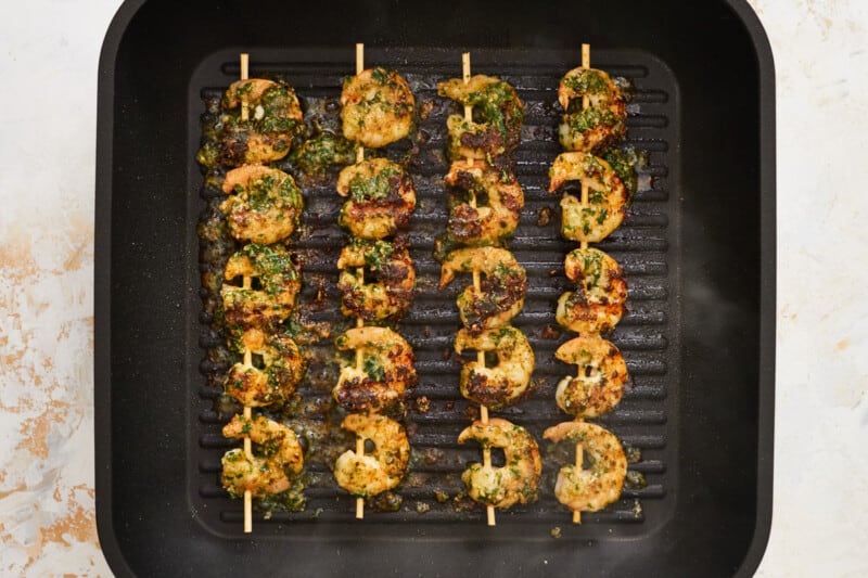 4 skewers of 5 each cooked pesto shrimp on a grill pan.