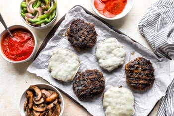 grilled burgers with sauce and vegetables on a baking sheet.