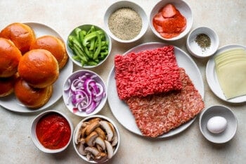 a plate of hamburger buns with meat, onions and other ingredients.