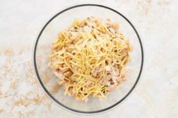cheese added to chicken filling in a glass bowl.