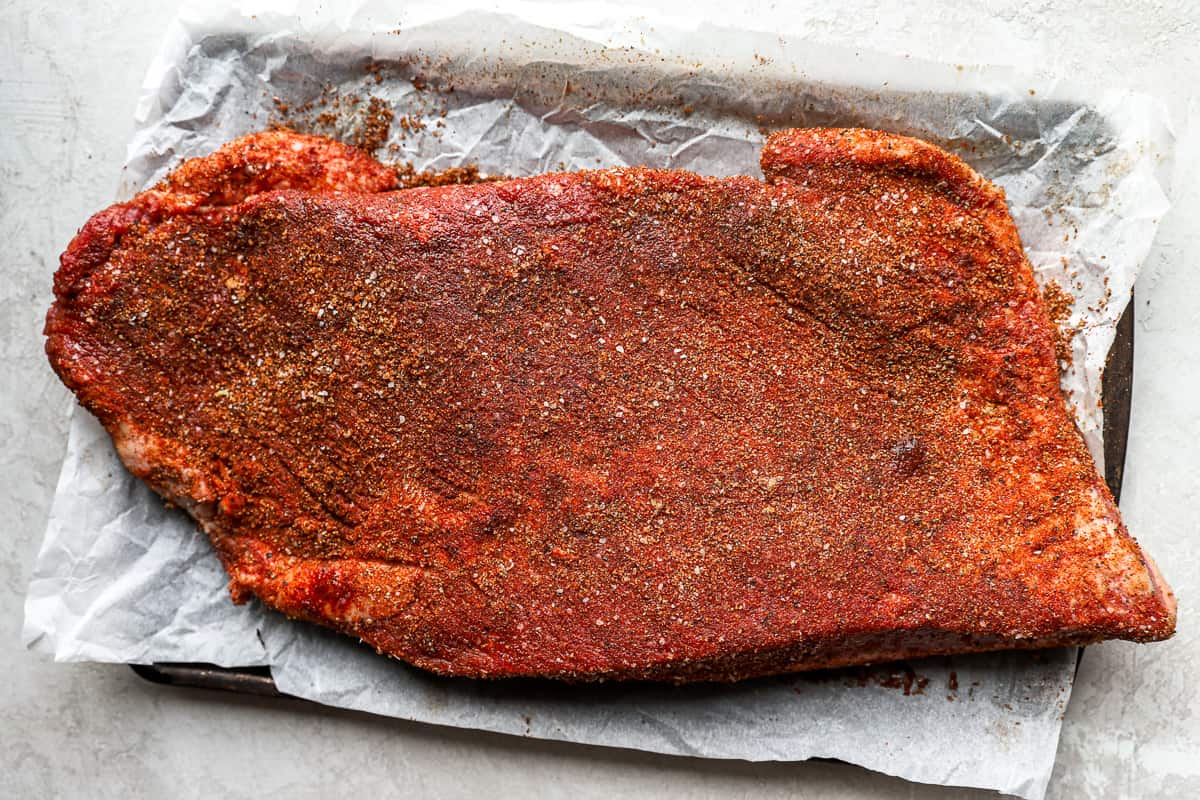 Seasoned, uncooked brisket on a parchment lined baking sheet.