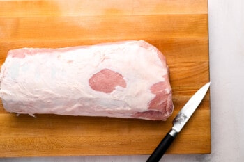 a raw pork loin roast on a cutting board with a knife.