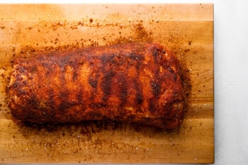 smoked pork loin roast seasoned with a dry rub on a wooden cutting board.