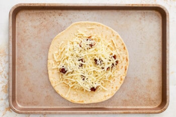 cheese sprinkled over sun dried tomatoes on a pizza crust.