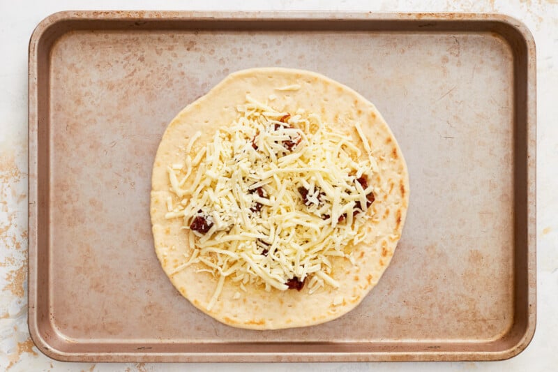 cheese sprinkled over sun dried tomatoes on a pizza crust.