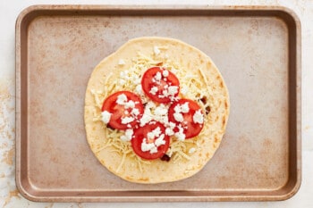 feta and tomatoes on top of sun dried tomatoes and cheese on pizza crust.