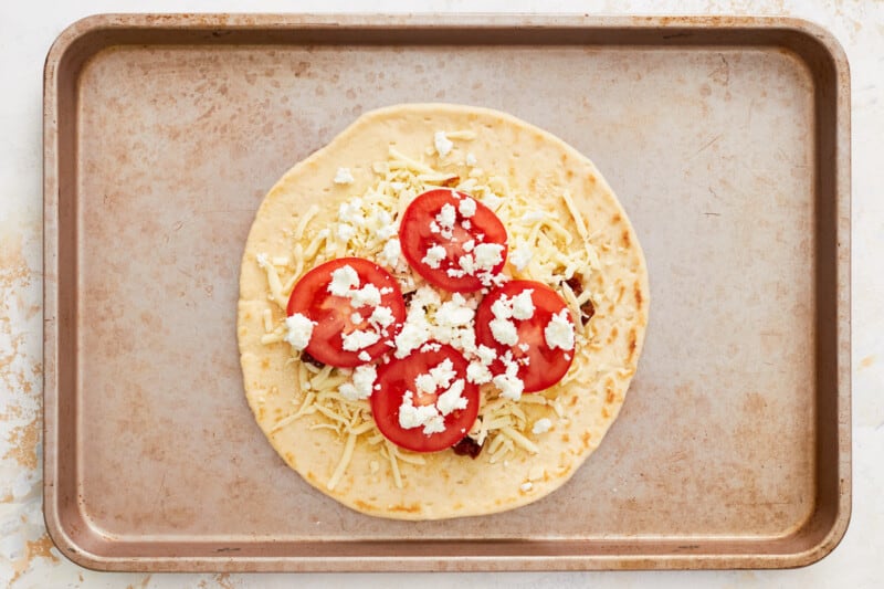 feta and tomatoes on top of sun dried tomatoes and cheese on pizza crust.