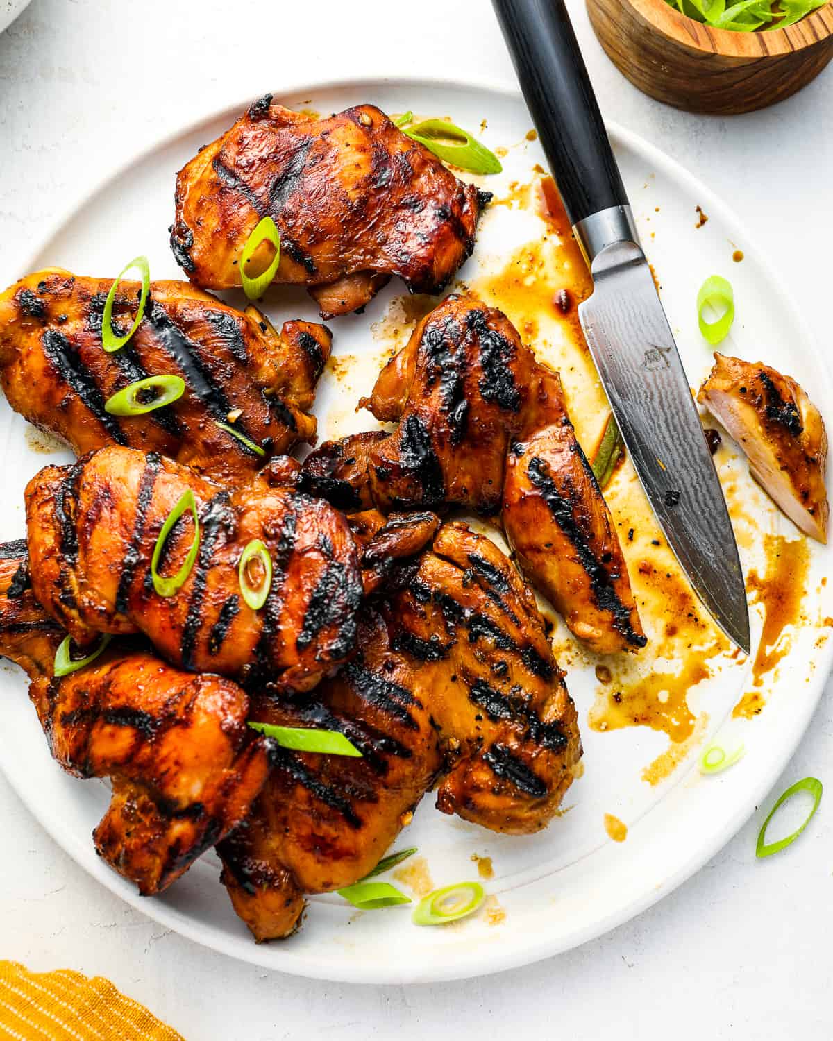 overhead view of a sliced chicken thigh on a white platter full of chicken thighs with a knife.